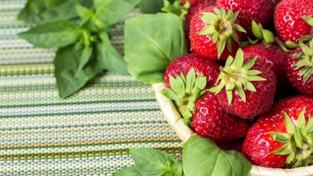 Fraises sucrées mûres dans un panier en osier et feuilles de menthe sur fond de bois