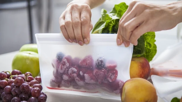 Une jeune mère met des framboises surgelées dans un sac transparent pour conserver les aliments. 