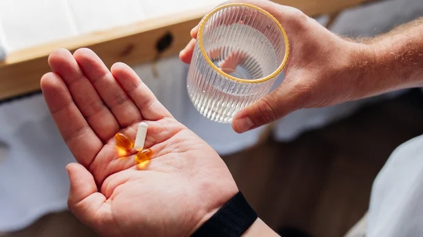 Gros plan sur une personne se préparant à prendre des suppléments vitaminiques avec un verre d'eau à la maison. Bien-être quotidien, routine de soins de santé et concept de soins personnels.